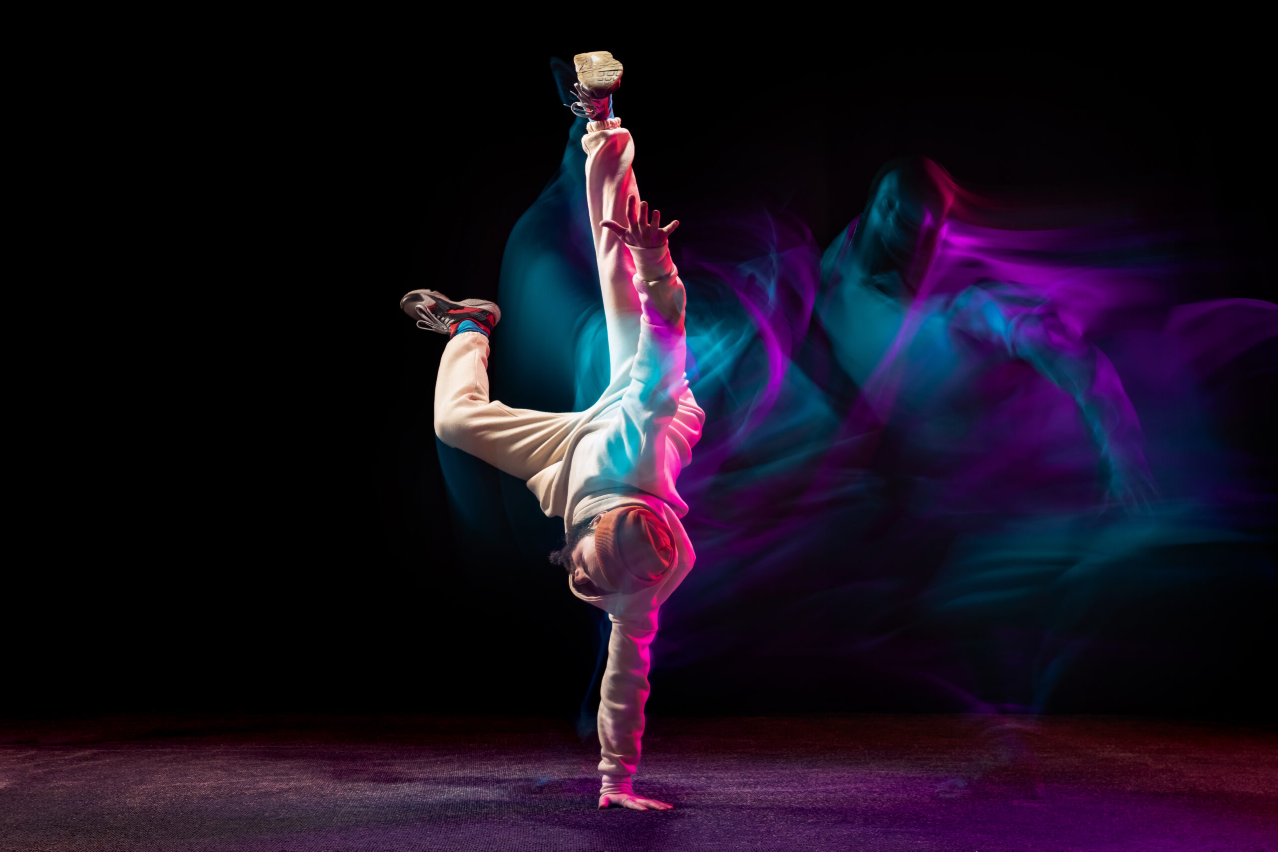 Young sportive man daancing breakdance isolared over black backgrounf in neon with mixed lights